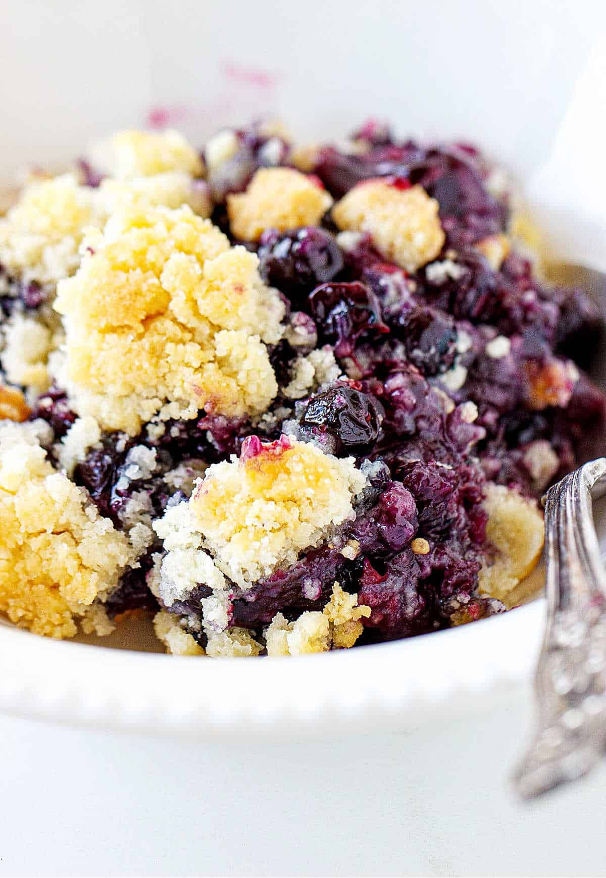 Crumbly blueberry dump cake serving in a white bowl with a silver spoon.