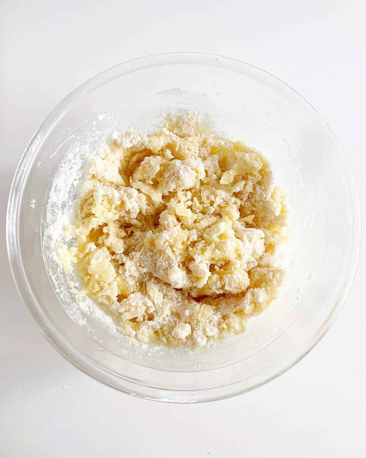 Glass bowl with crumbly topping mixture for dump cake. White surface.