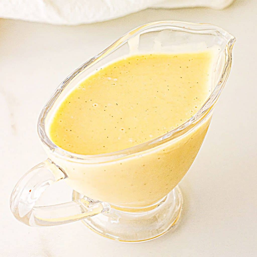 Glass sauce boat with yellow custard cream on white surface