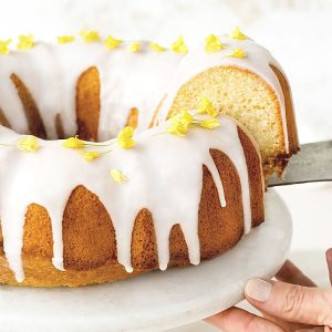 Close up of glazed lemon bundt cake with a cut slice on a white plate.