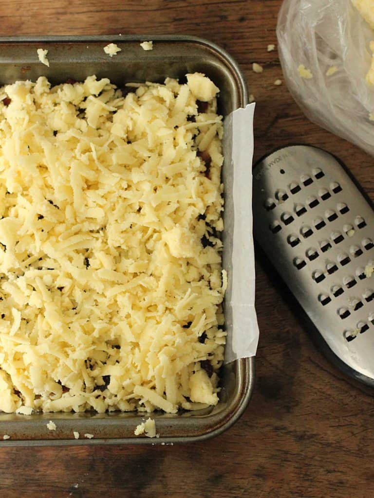 Grater and metal pan with unbaked shortbread on wooden table