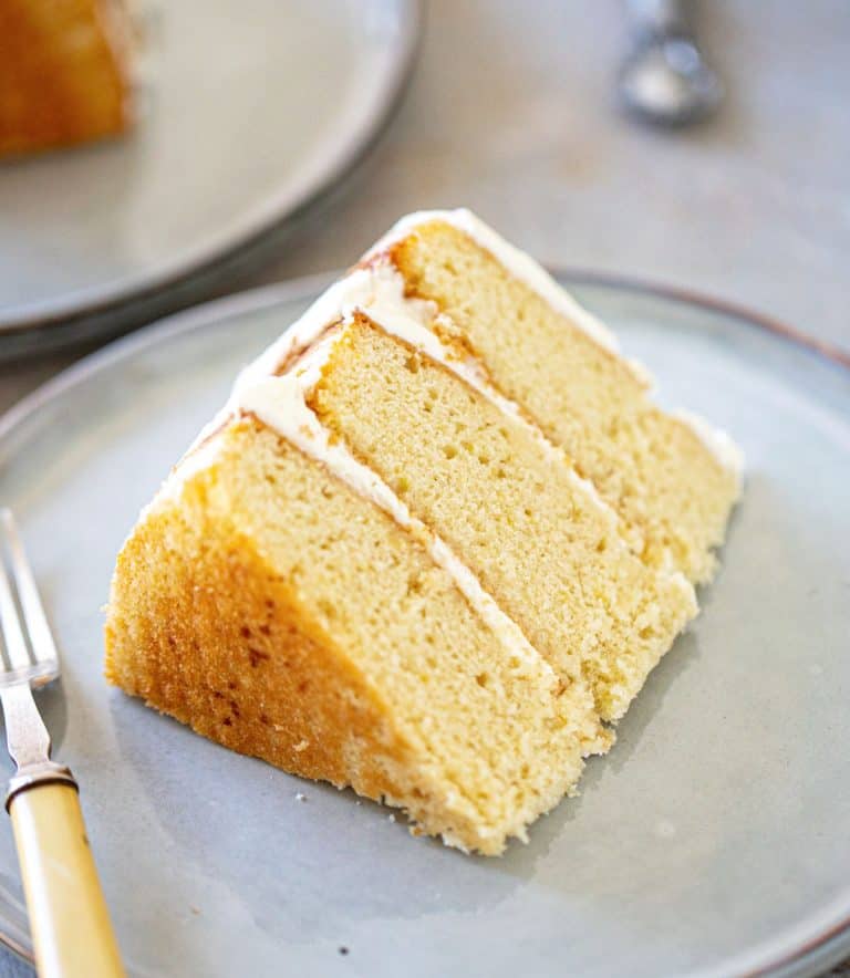 Close of slice of three layer lemon cream cake on grey plates and background