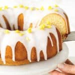 Yellow and brown text overlay on image of glazed cake being cut on a white cake stand.