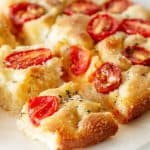 Close up of round tomato focaccia bread cut in squares on white surface