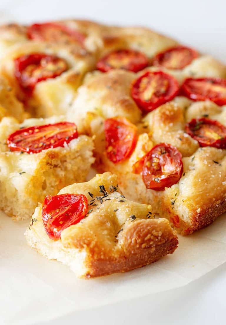 Close up of round tomato focaccia bread cut in squares on white surface