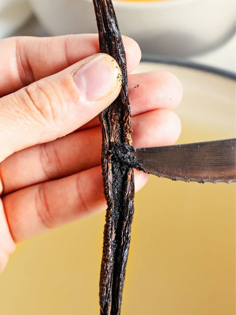 Scraping seeds from half a vanilla bean with the tip of a knife.