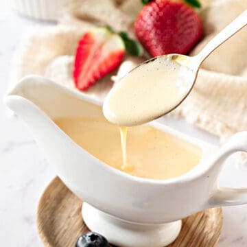 Close up spooning creme anglaise from a white saucer. Beige cloth, strawberries.