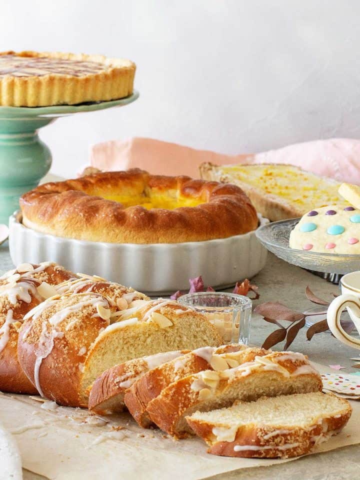 An Easter brunch table with a pie on a green stand, cookies, braided breads, a pie, a cup of tea.