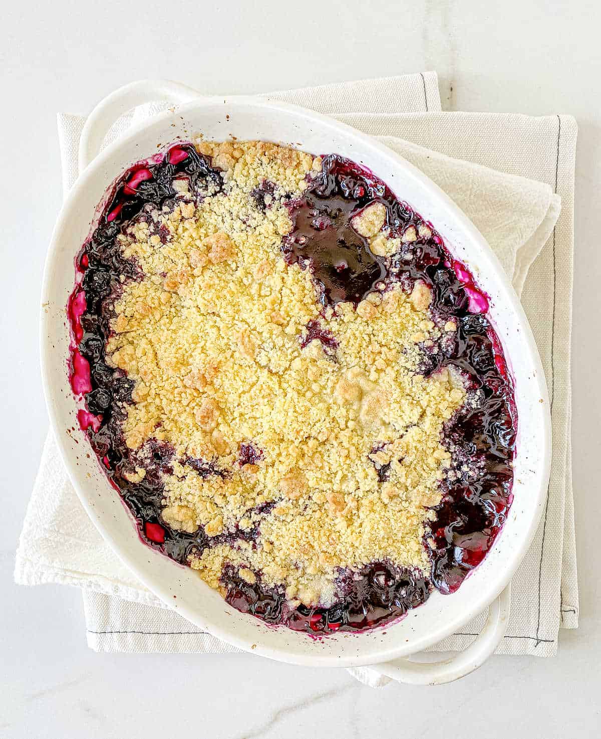 Top view of baked blueberry crumble in oval white dish on white surface