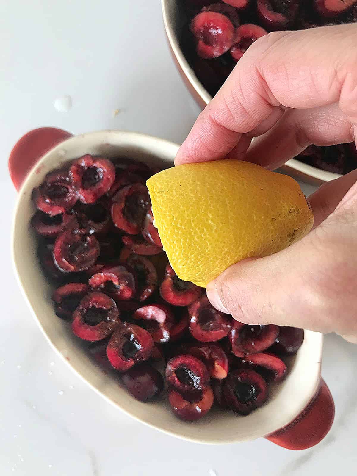 Adding lemon juice to fresh cherries in oval dish on white surface