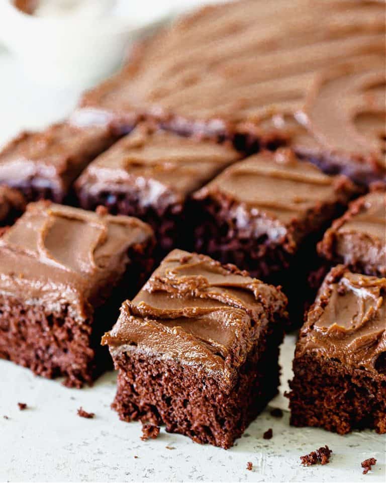 Squares of chocolate potato cake on light blue surface, small white bowl in background
