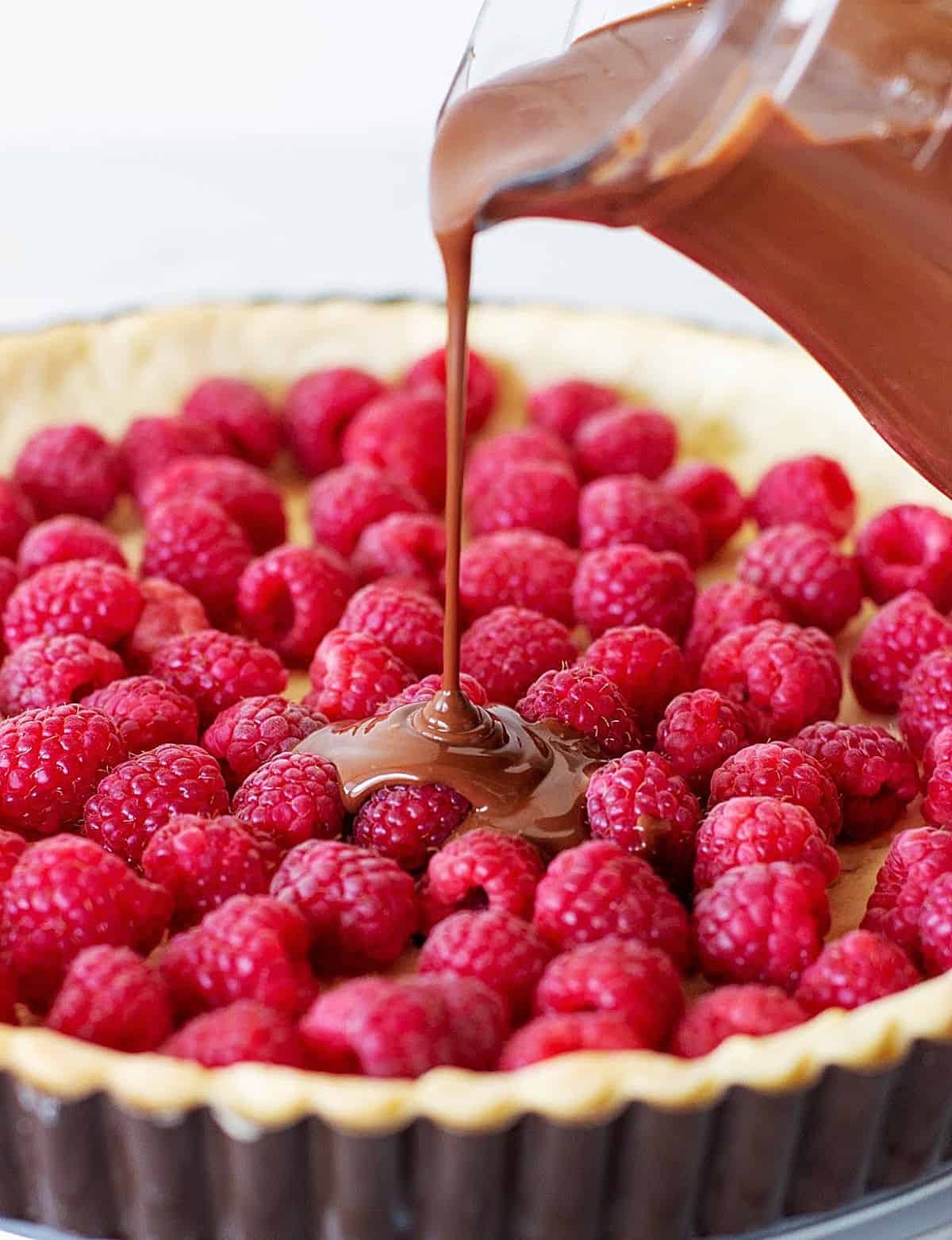 Pouring chocolate filling onto tart crust filled with fresh raspberries