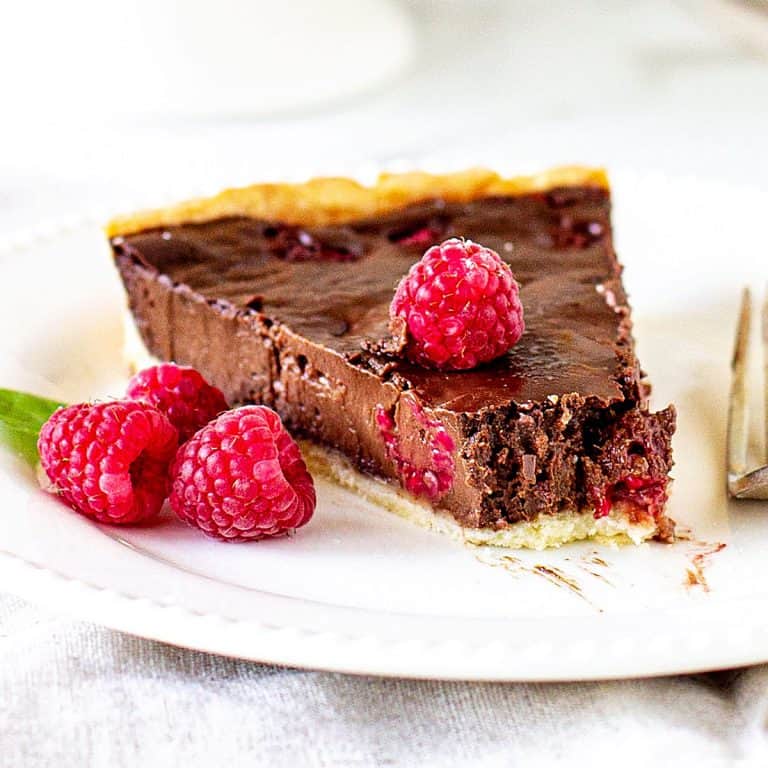 Single slice of raspberry chocolate tart on white plate, whole raspberries, white background.