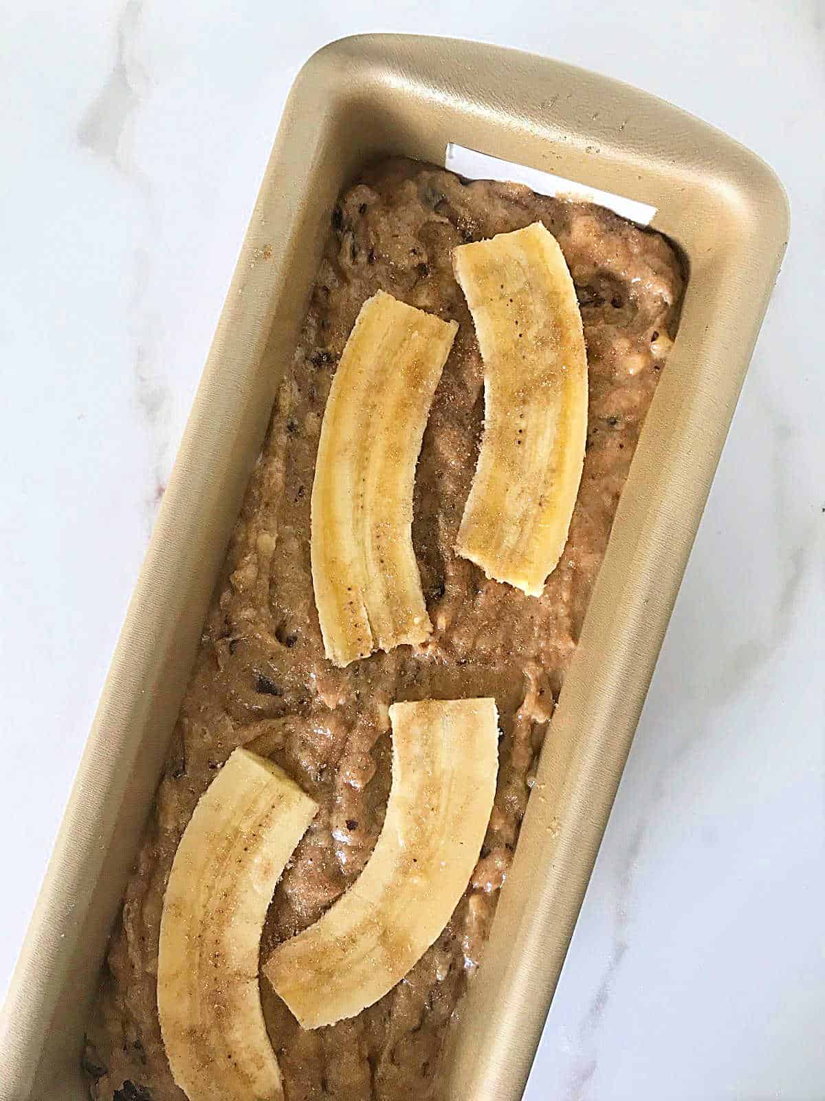 Banana bread batter with whole banana on top in metal pan on marble surface.