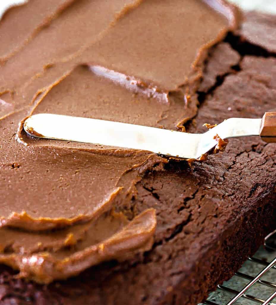 Spreading chocolate peanut frosting with an offset spatula on a chocolate cake.