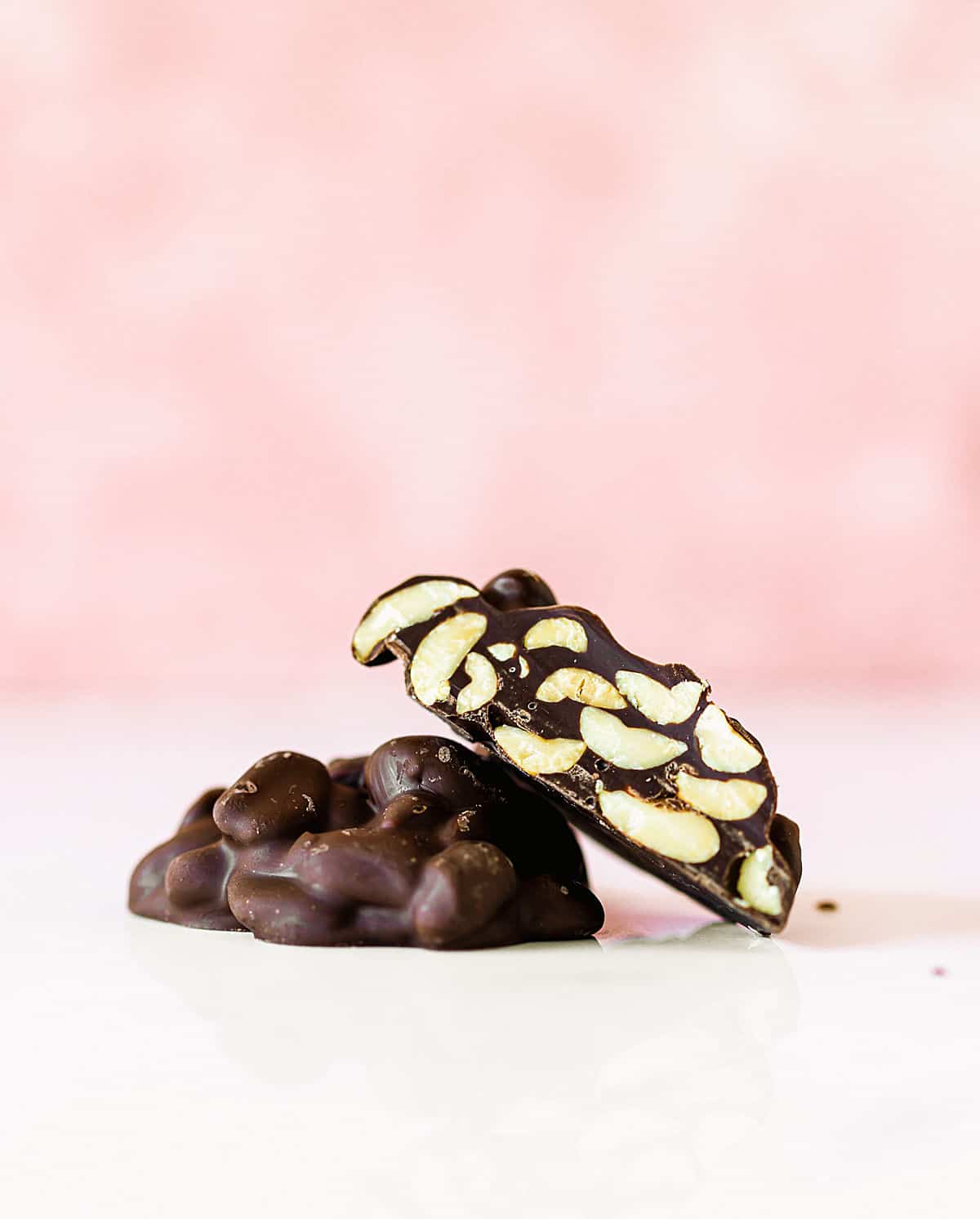 Cut and whole chocolate peanut clusters on white and pink background