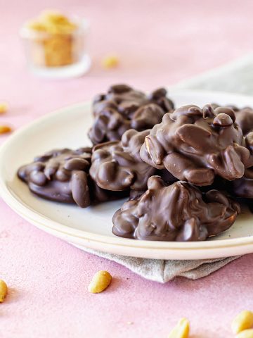 White plate with chocolate peanut clusters on pink surface, peanuts around