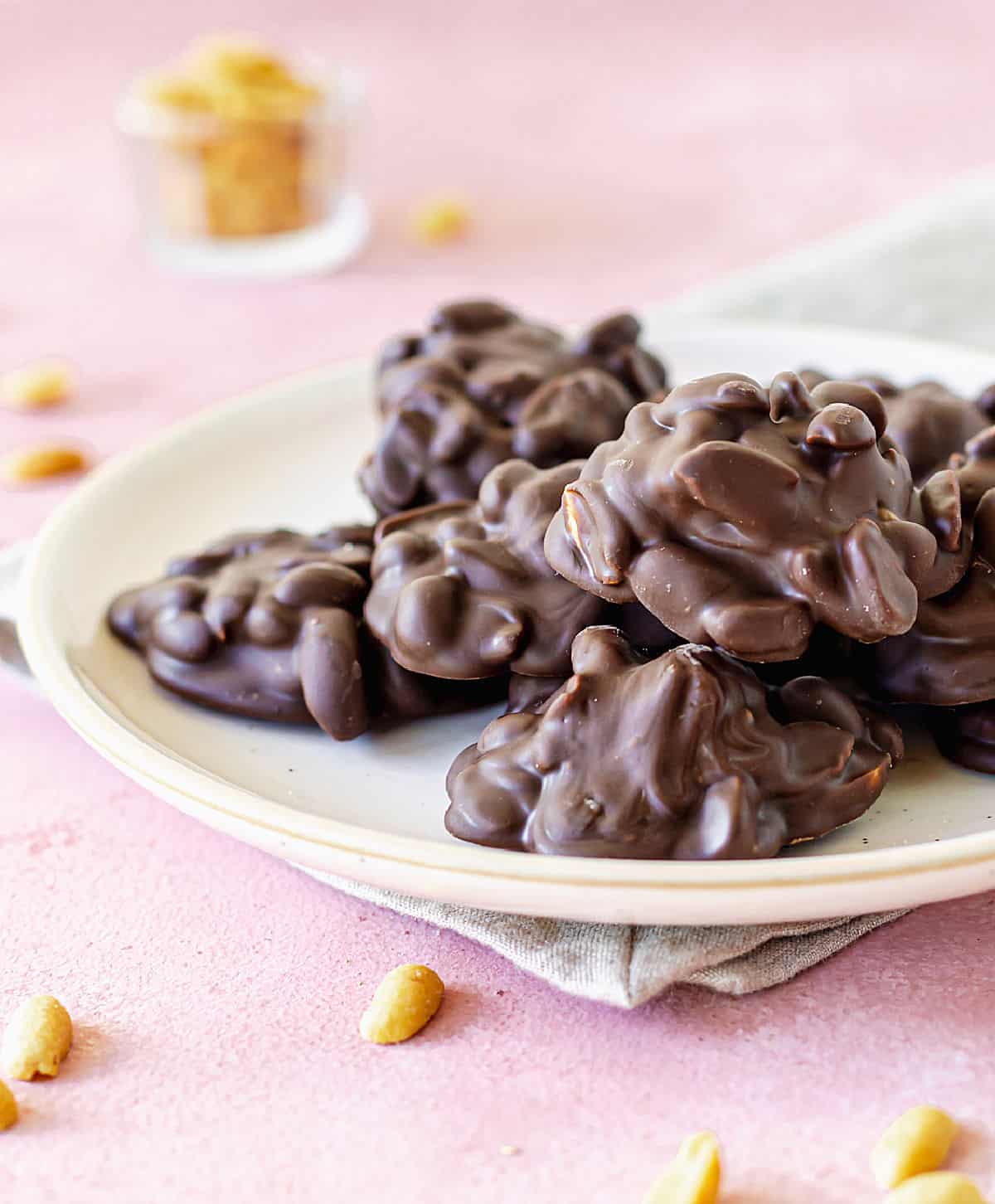 White plate with chocolate peanut clusters on pink surface, peanuts around