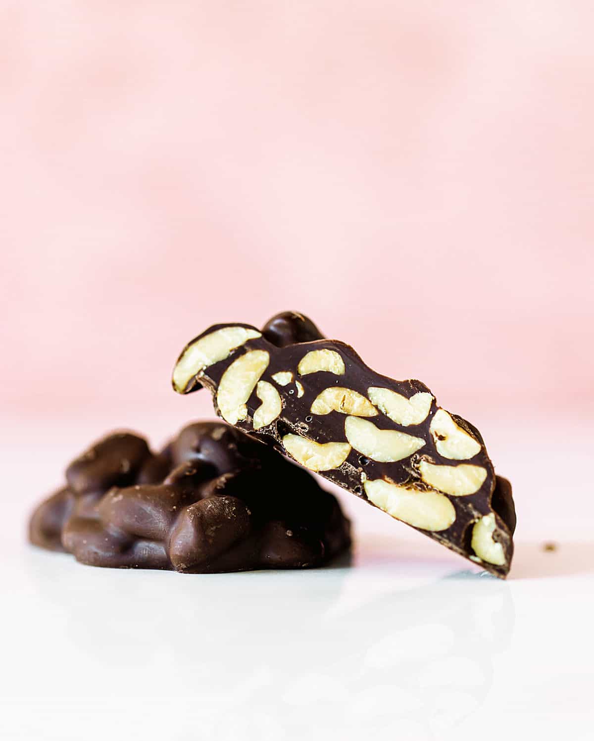 Cut and whole chocolate peanut clusters on white and pink background.