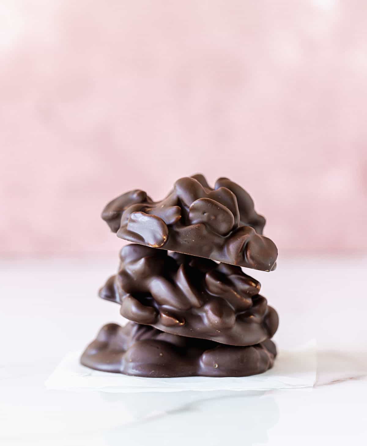 Stack of three chocolate peanut clusters on white and pink background.