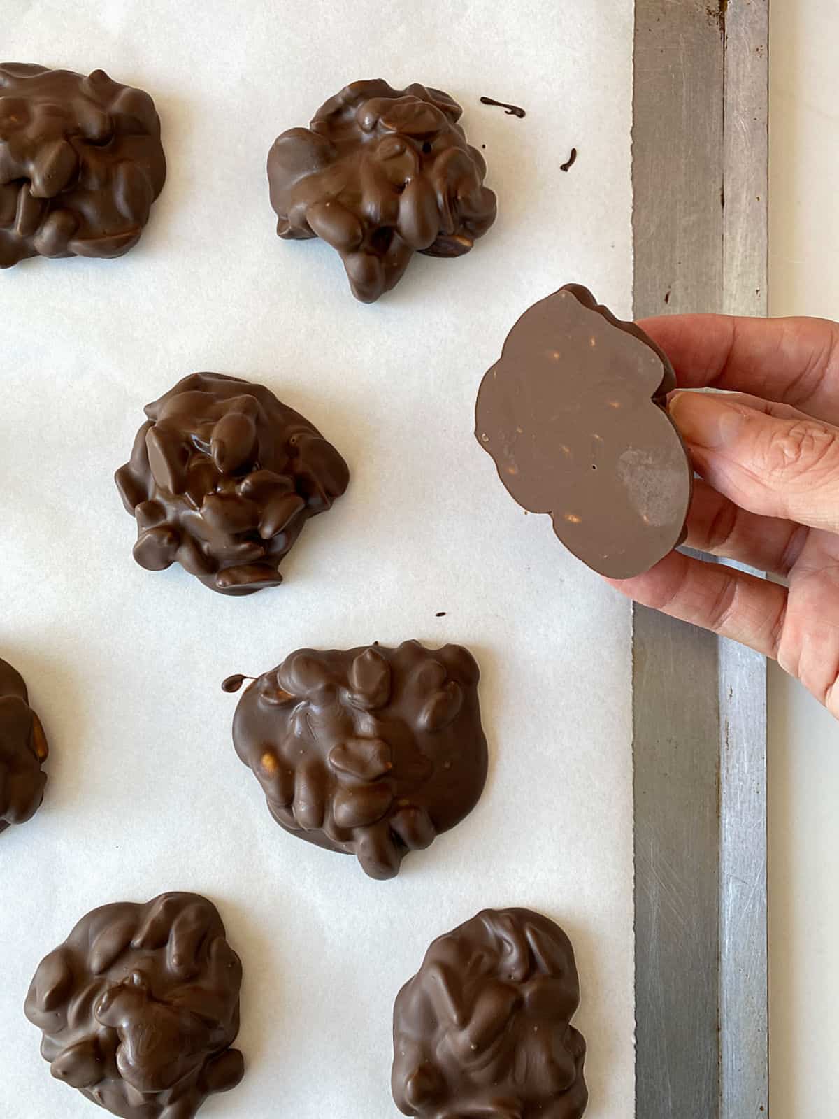 Several chocolate peanut clusters on white parchment and hand showing bottom of one of them