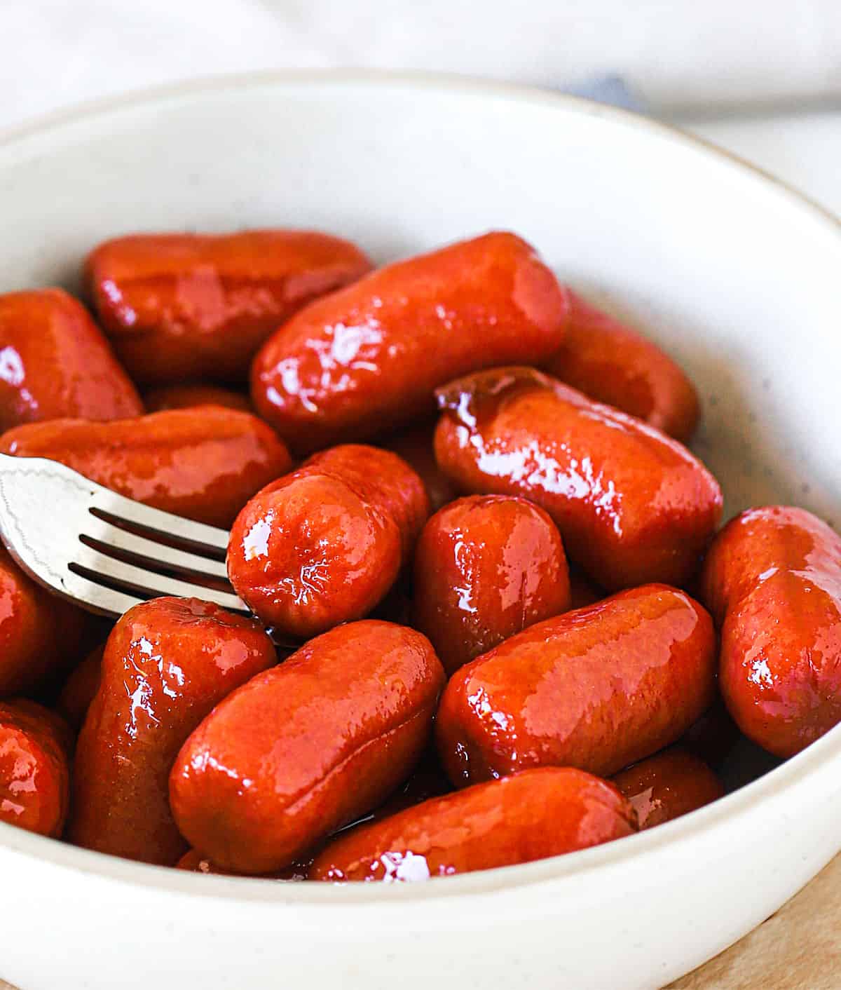 Close up of mini sausages in white bowl, a fork 