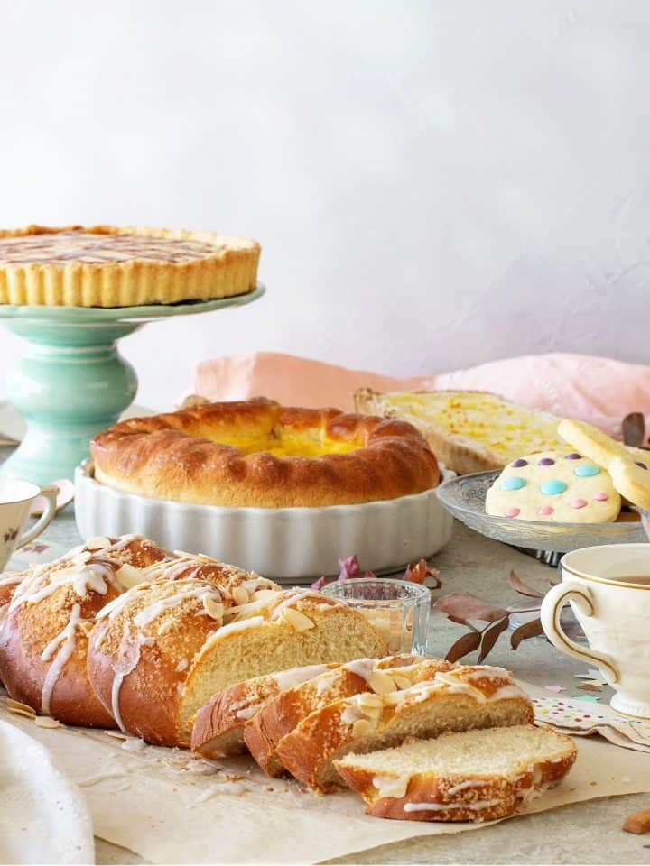 An Easter brunch table with a pie on a green stand, cookies, braided breads, a pie, a cup of tea