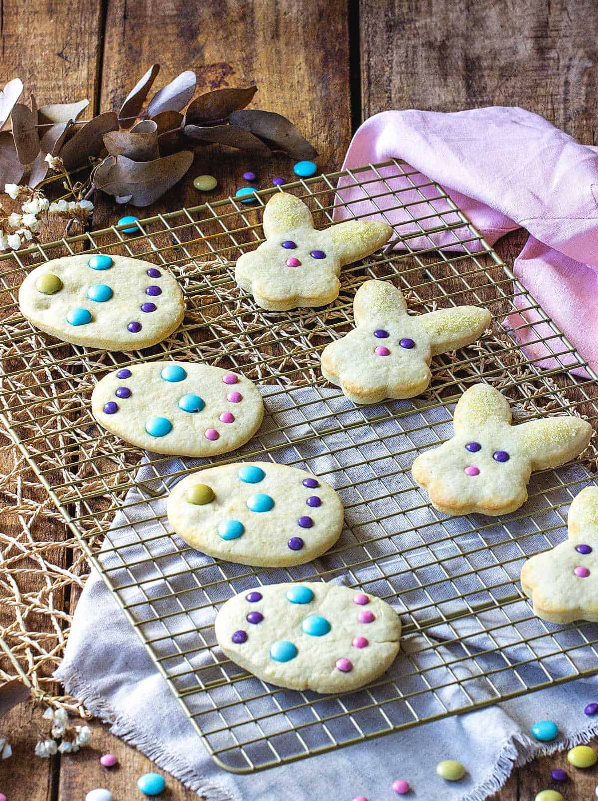 Several Easter sugar cookies on wire rack over wooden table with linens.