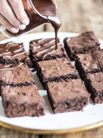 Several brownie squares on white plate, hand pouring chocolate sauce