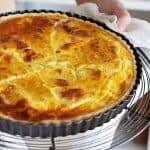 Hands holding whole ham and cheese quiche in metal pan