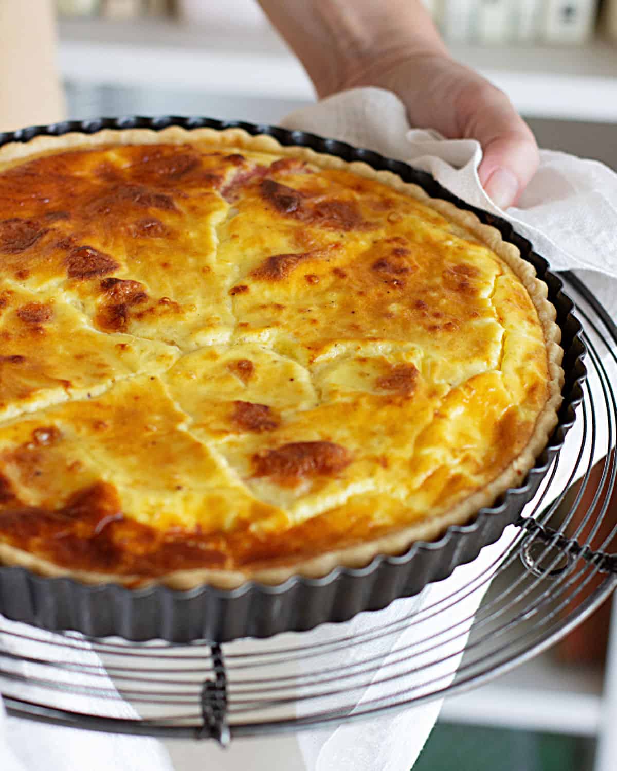 Hands holding whole ham and cheese quiche in metal pan