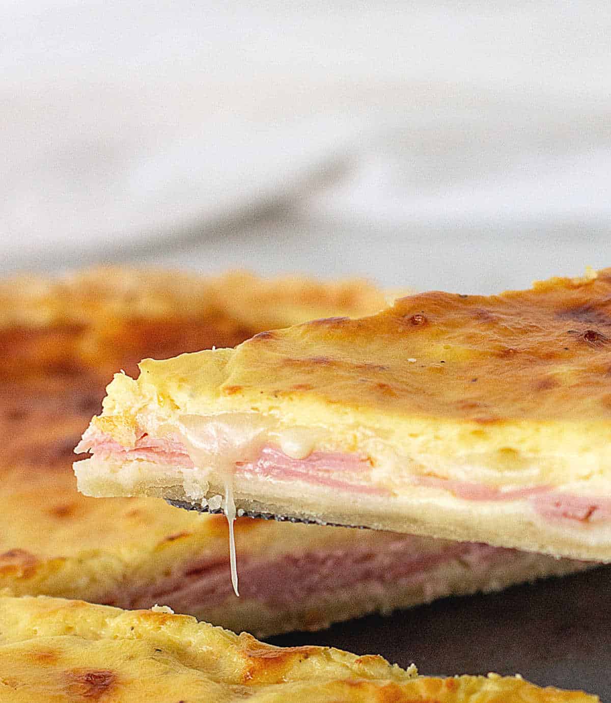 Lifting slice of ham and cheese quiche, melting cheese