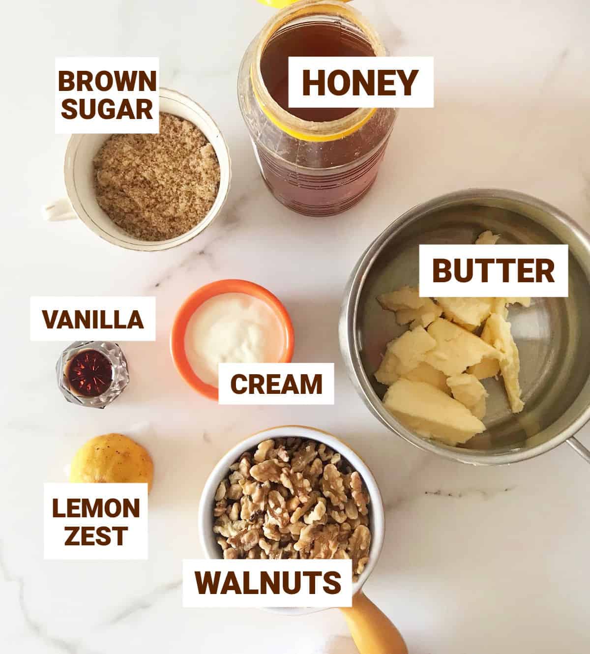Honey walnut bars ingredients in bowls on white surface, including lemon, cream and brown sugar