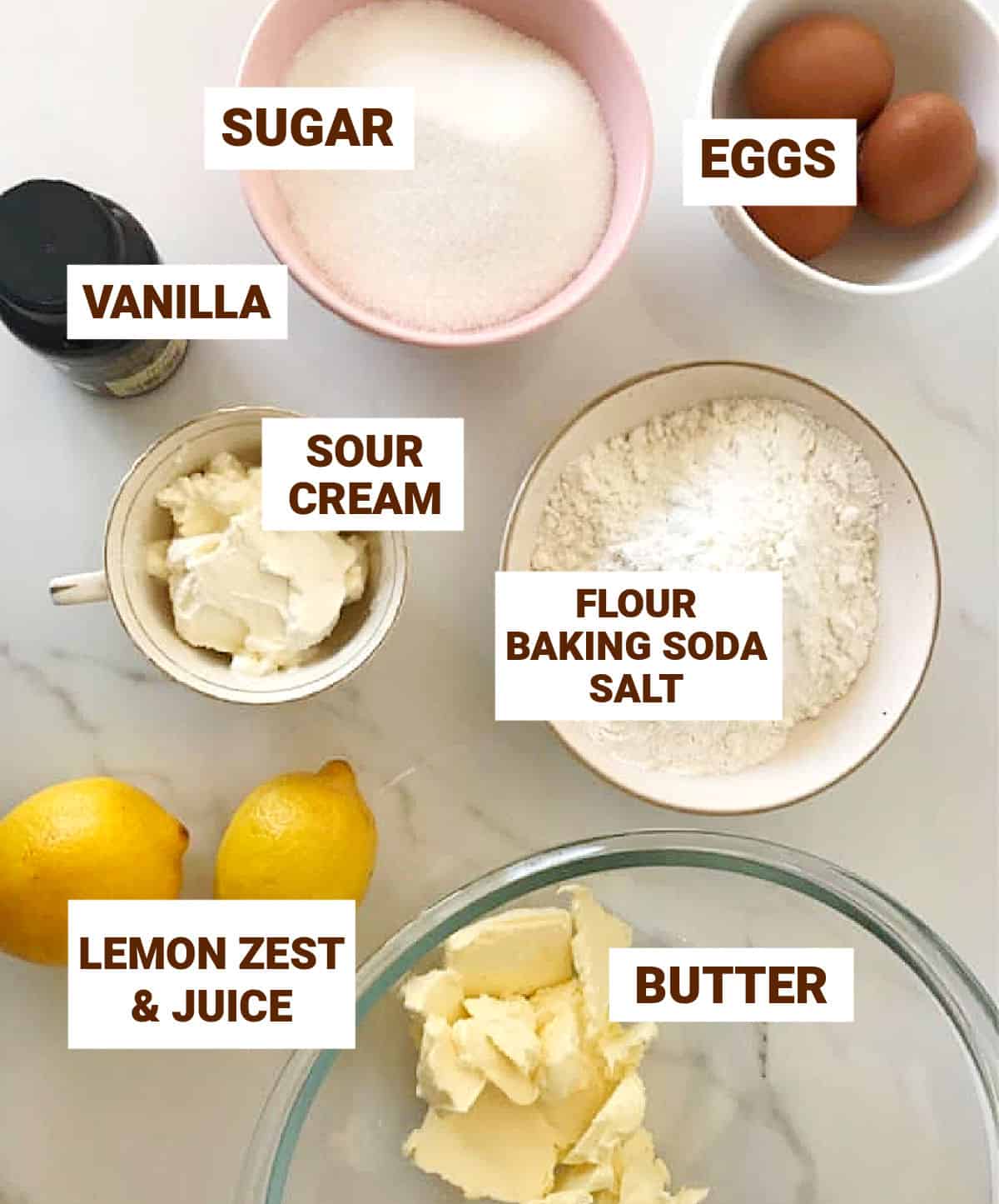 Lemon Pound Cake ingredients in bowls on white surface, including lemons, eggs, sour cream and vanilla.