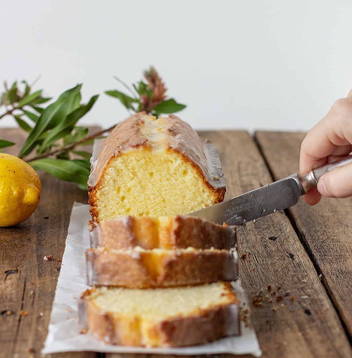 Cutting pound cake slices on a wooden board, lemon and leaves as props