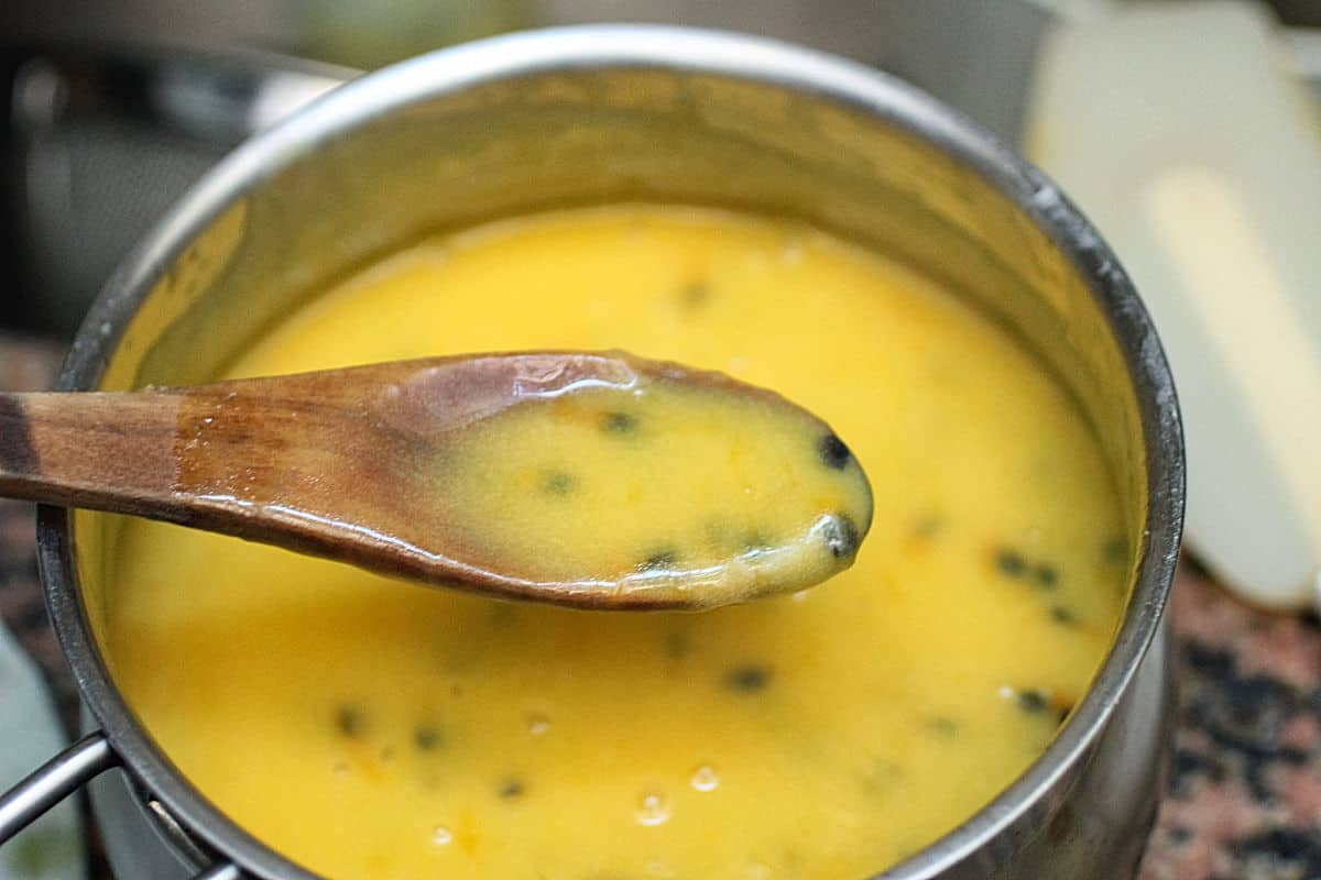 Spooning passion fruit curd from metal saucepan