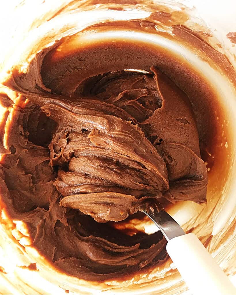 Glass bowl with peanut butter chocolate frosting. White silver spoon inside. Top view.