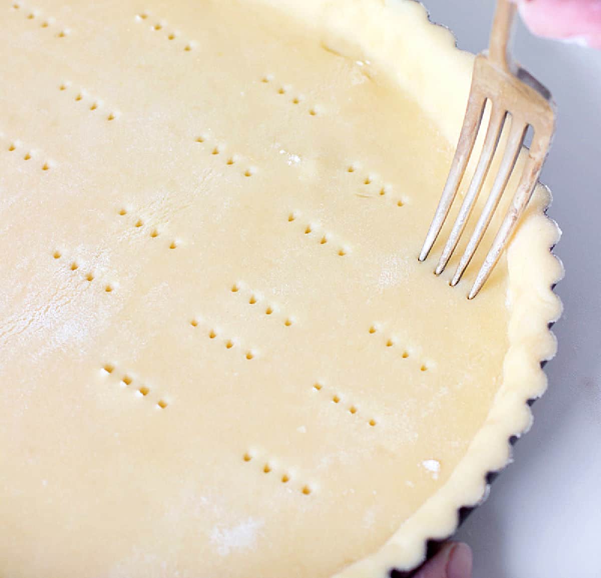 Pricking tart crust with fork, white counter.