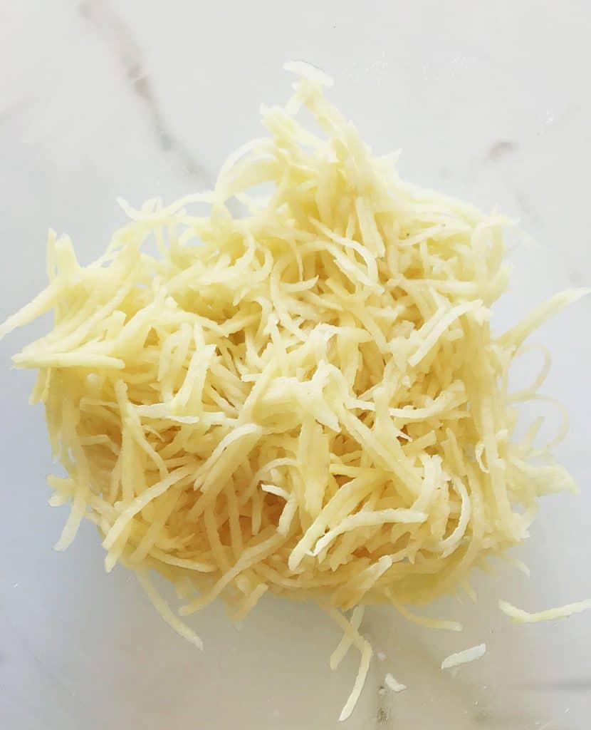 Shredded raw potato on white marble surface