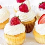 Vanilla cupcakes topped with cream and fresh strawberry on white plate
