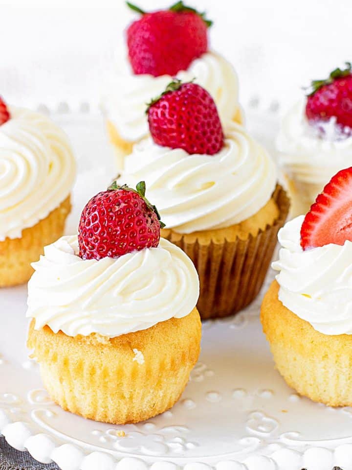 Vanilla cupcakes topped with cream and fresh strawberry on white plate