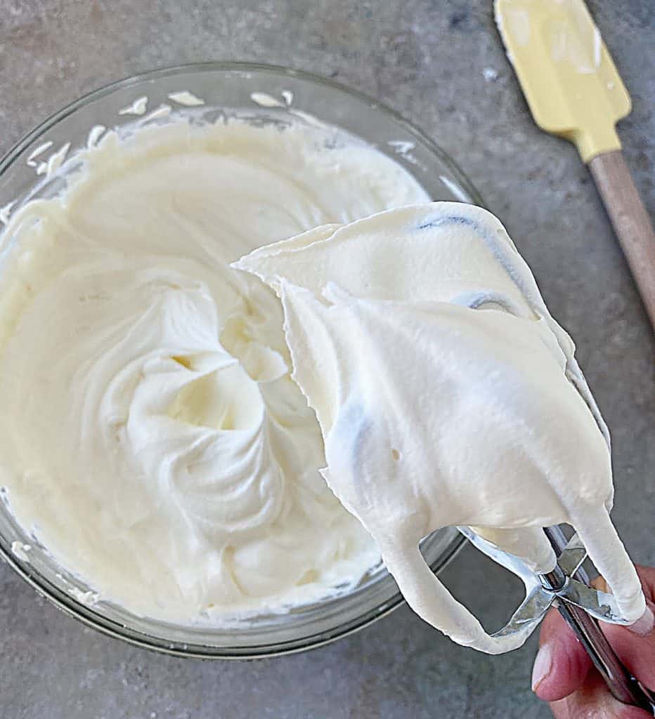Beaters with dollop of whipped cream, bowl on grey table beneath it