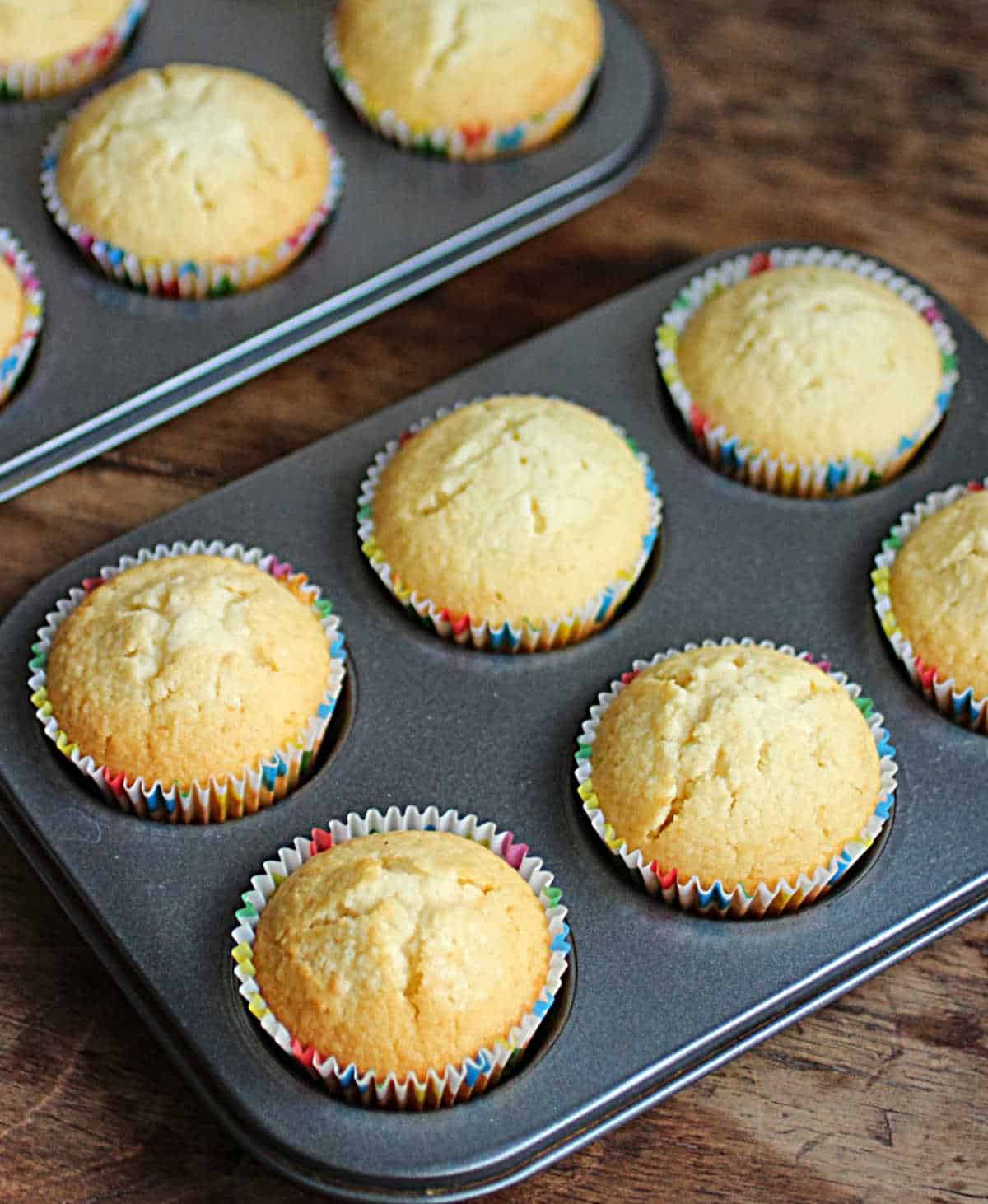 Top view of baked coconut cupcakes in metal muffin pans on wooden table