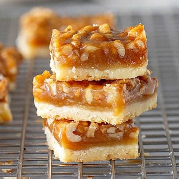 Close up of stack of walnut squares on wire rack, loose walnuts, grey surface