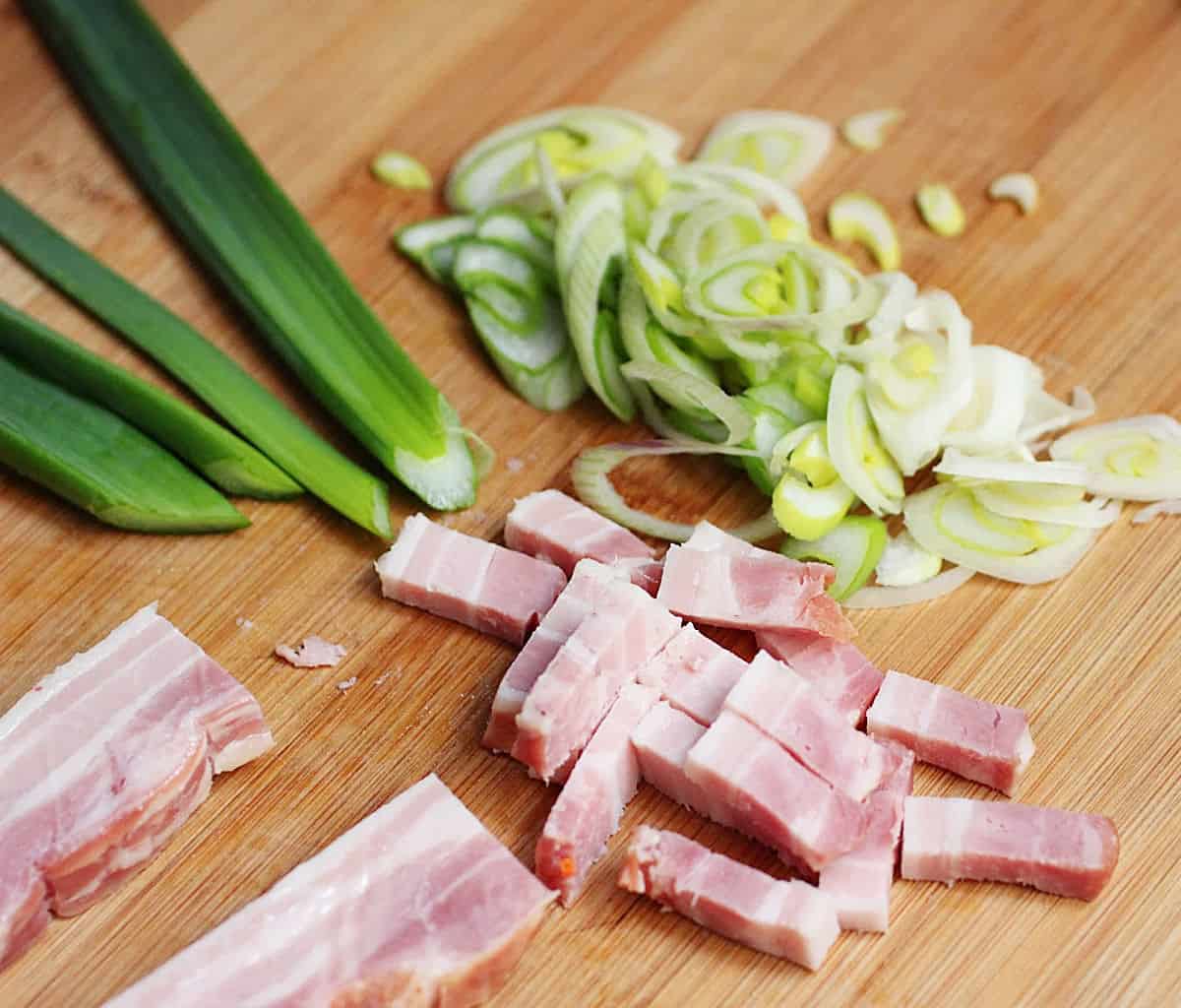 Wooden board with bacon strips and sliced green onion