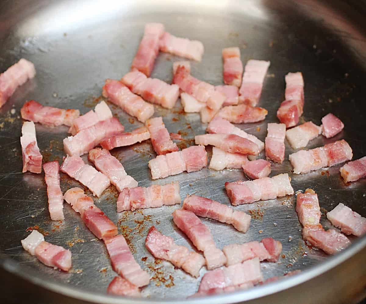 Thick cut bacon strips rendering in metal skillet