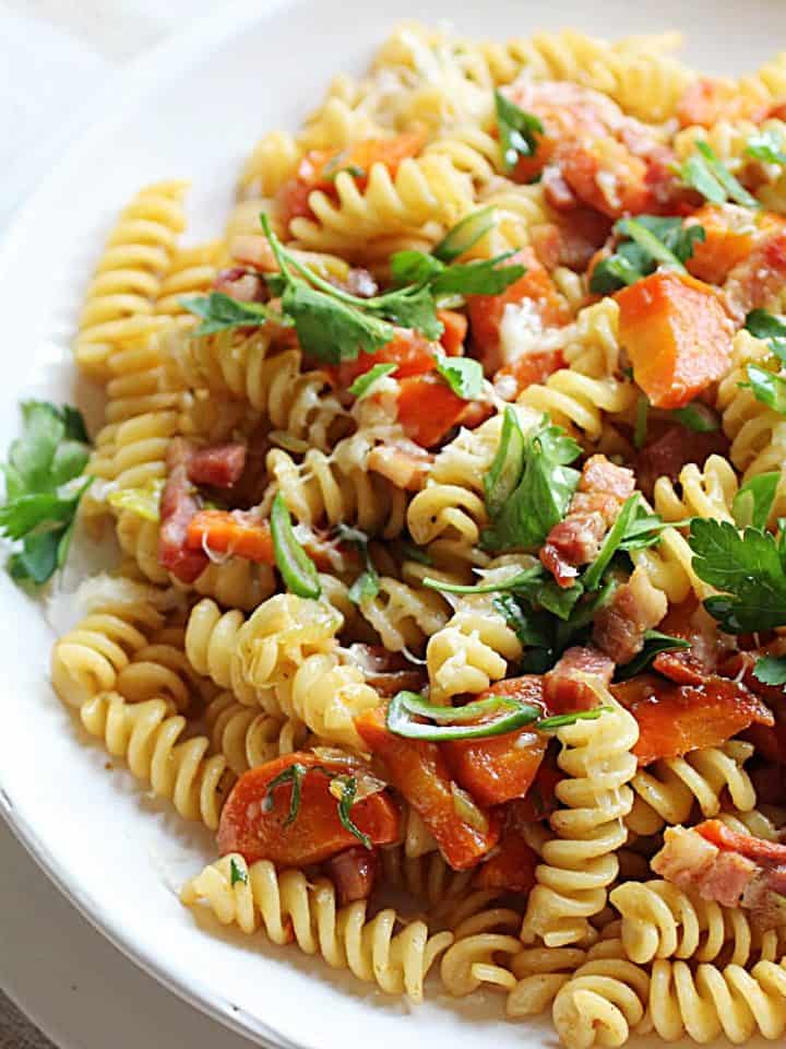 White plate with fusilli pasta, carrots, bacon and chopped parsley