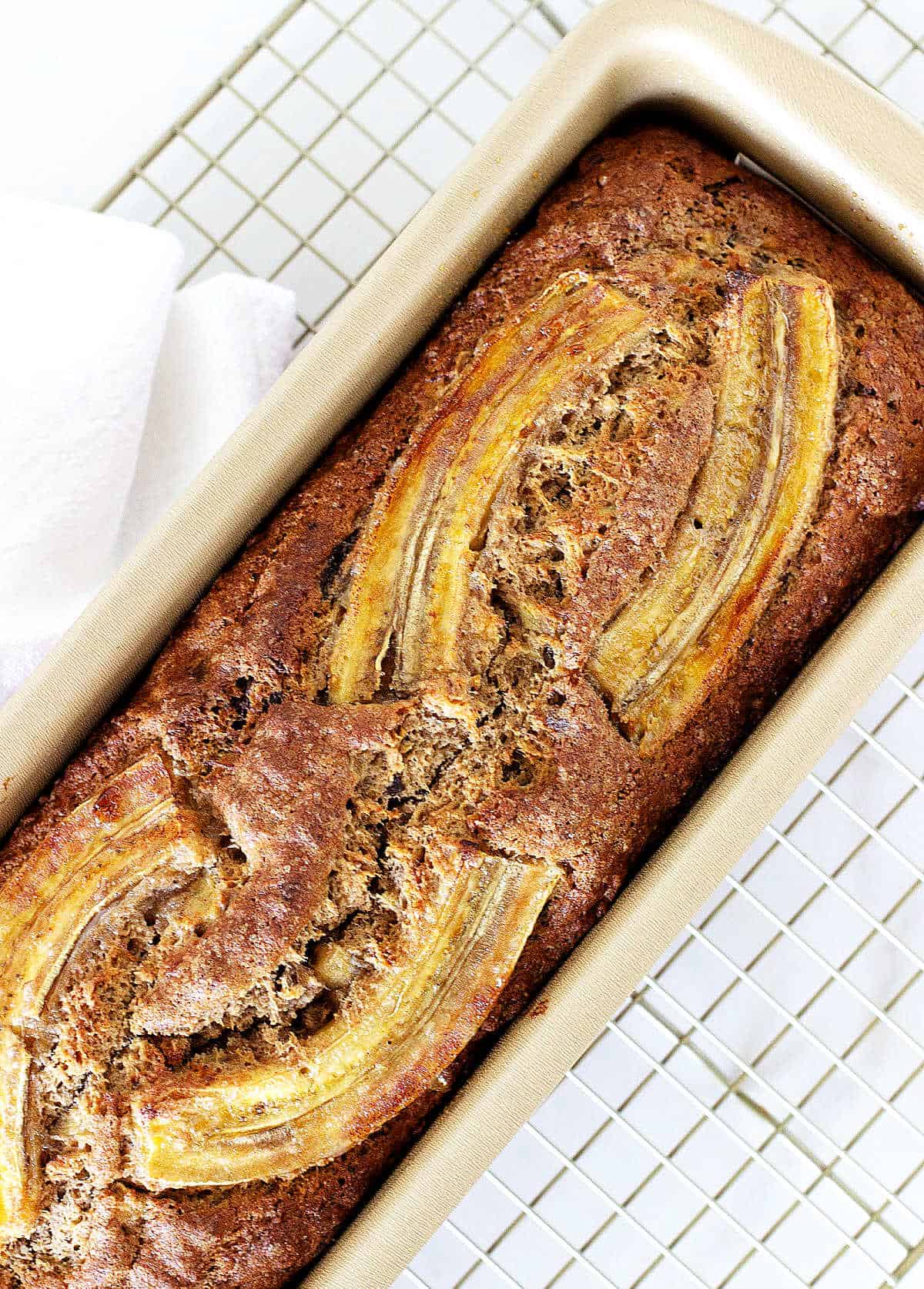 Top view of banana bread in metal pan on white kitchen towel.