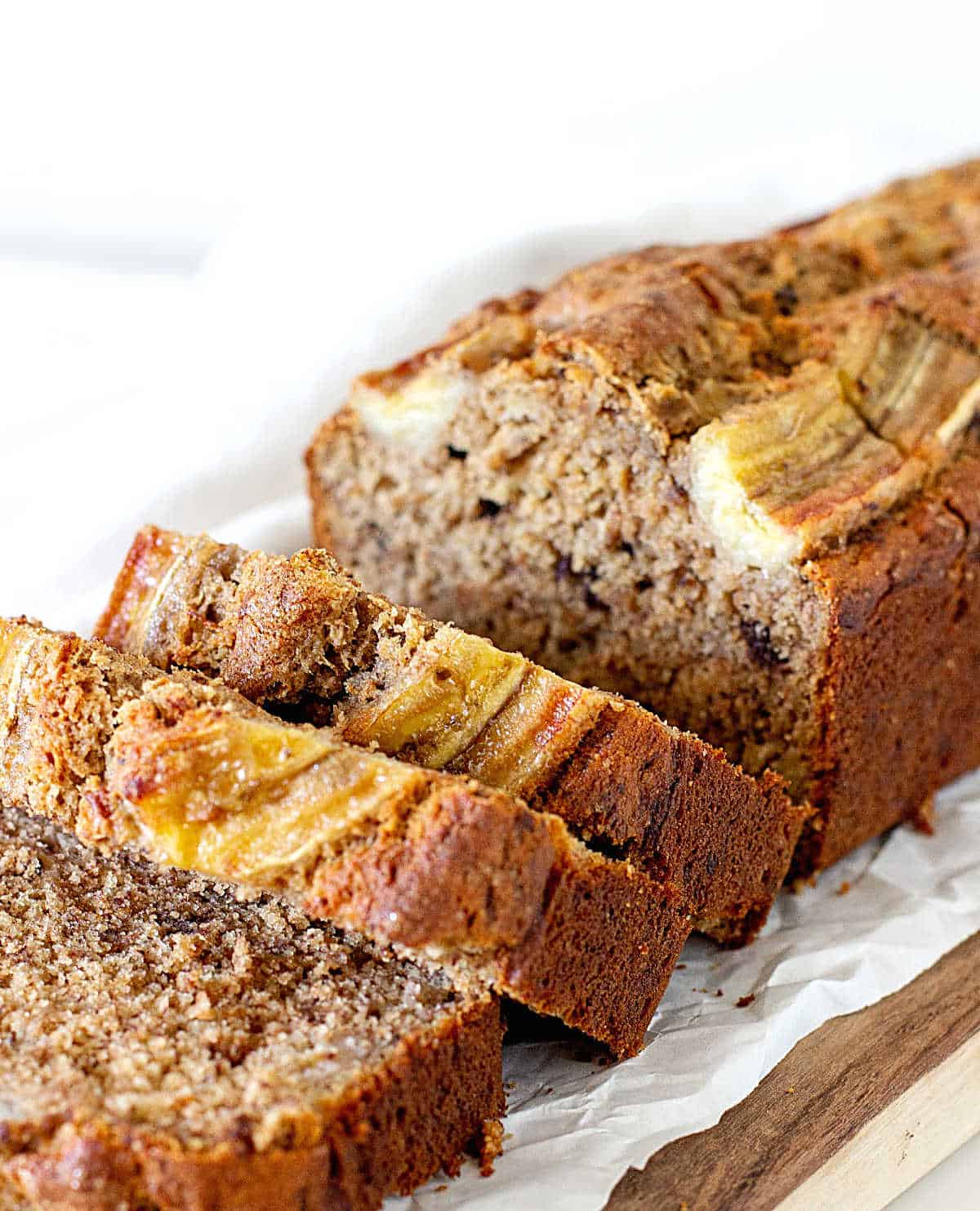 Sliced banana bread loaf on white parchment paper on a white background. 