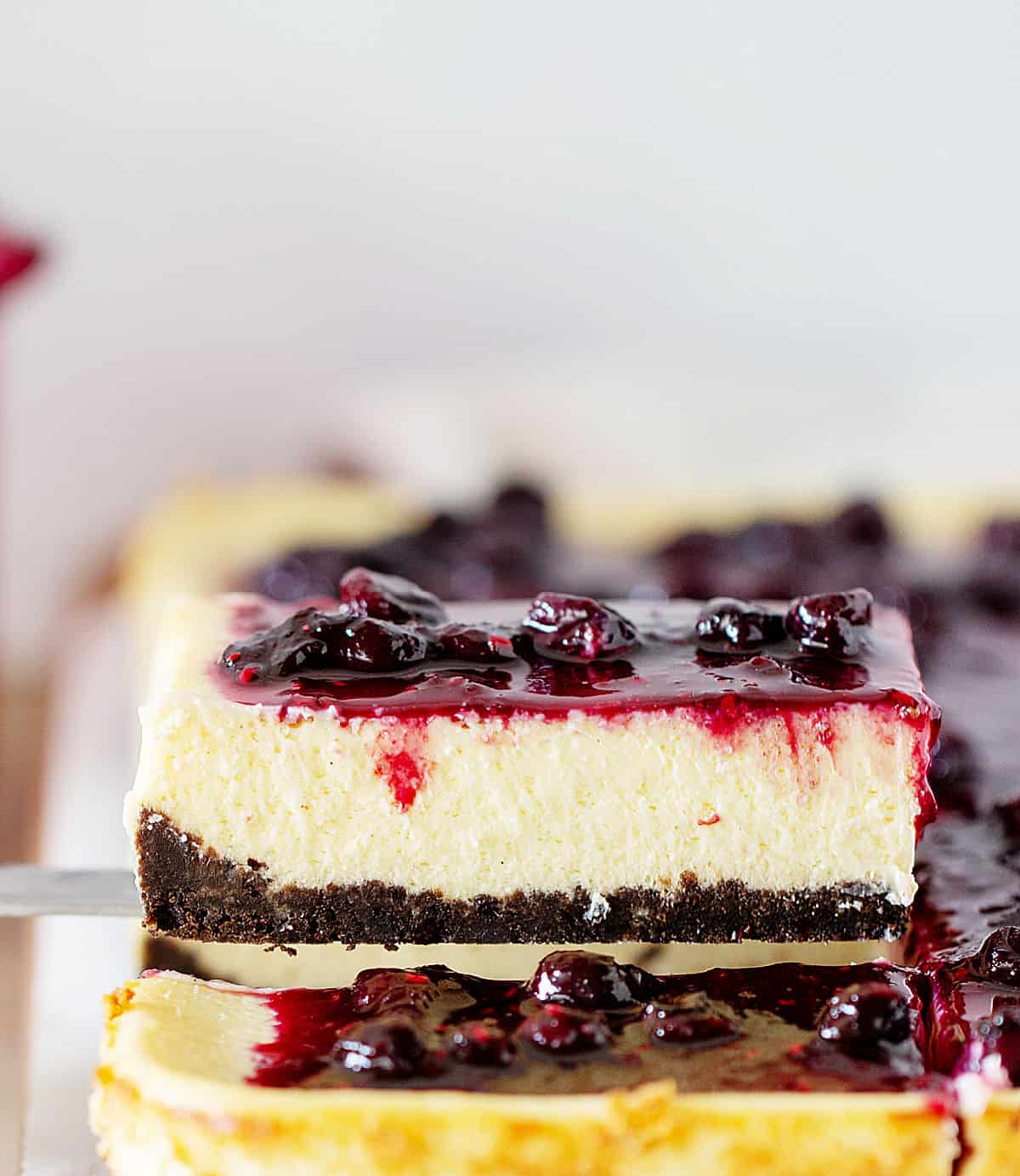 Slice of berry topped cheesecake being lifted from whole cake